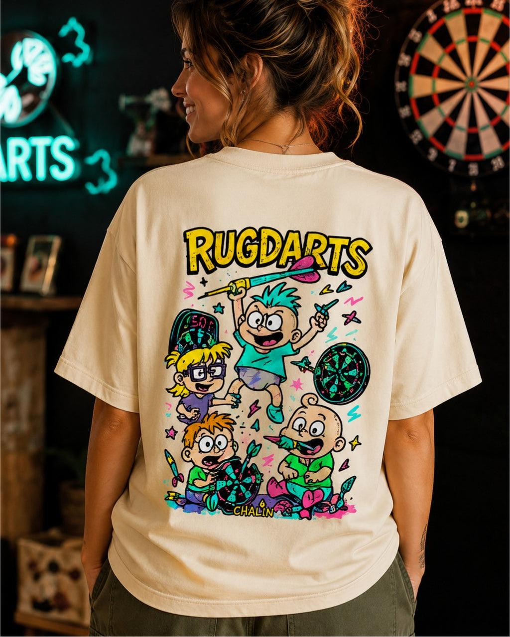 Chica de espaldas con la camiseta de dardos Rugdarts beige y el diseño de bebés con dardos en la espalda