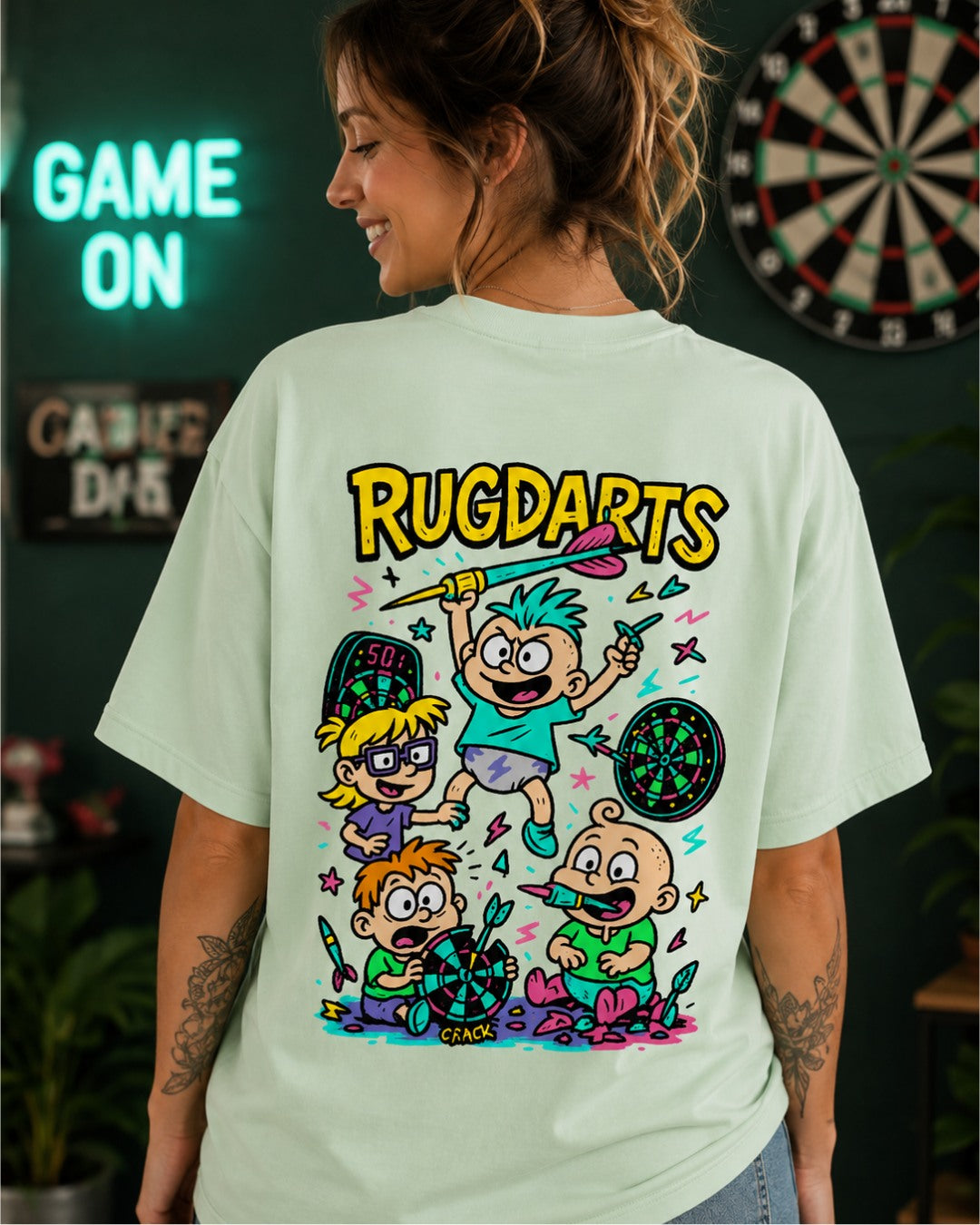 Chica de espaldas con la camiseta de dardos Rugdarts verde menta y el diseño de bebés con dardos en la espalda